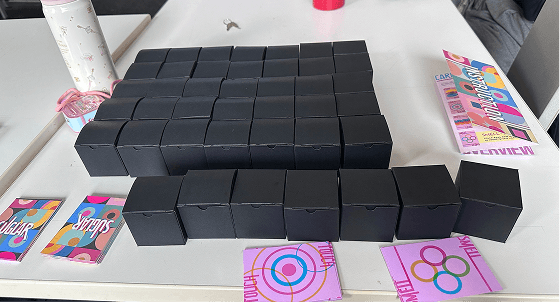 Rows of small black boxes assembled by hand, with printed sensory cards and the instruction sheet beside them