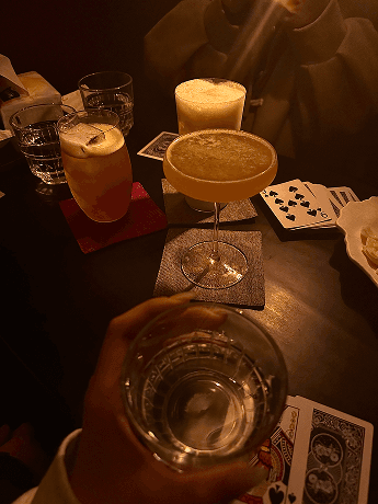 Original phone photo of a dark bar table with drinks and playing cards